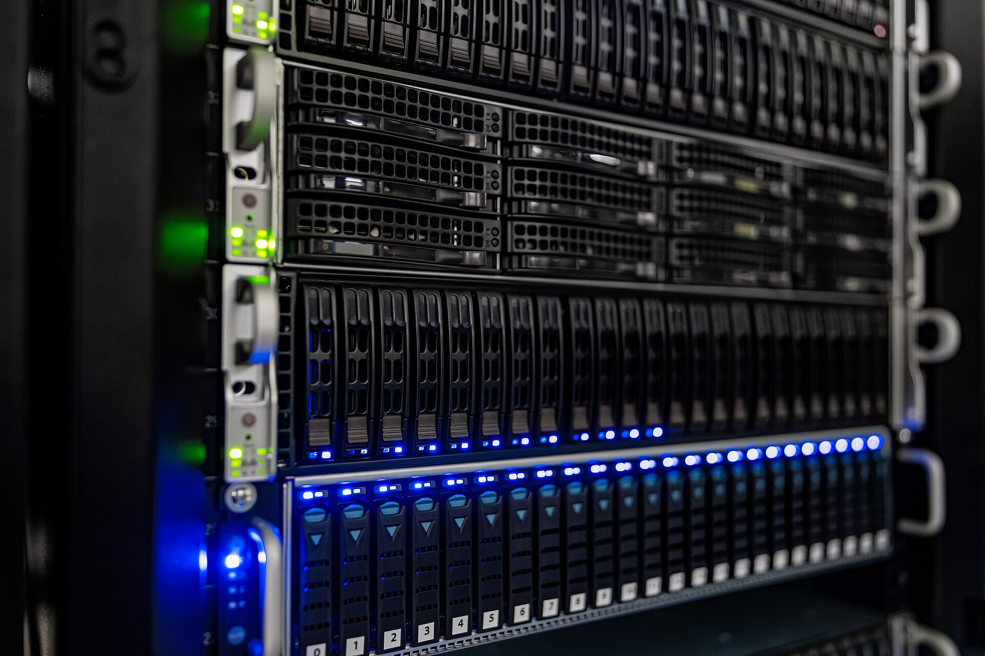 Serveurs empilés dans une baie informatique, voyants bleus et verts allumés devant des rangées de disques